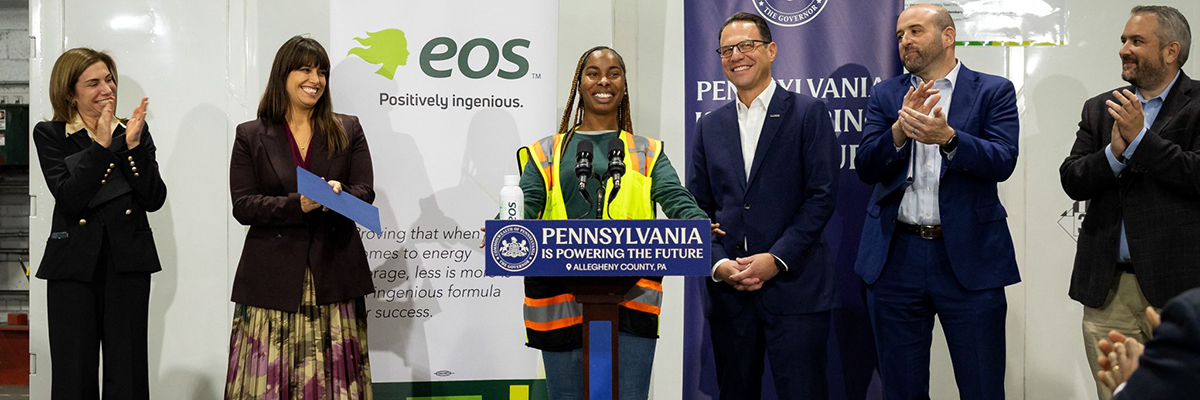 Woman in yellow work vest standing in front of podium with people clapping behind her